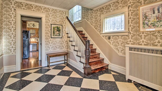 A hallway with a checkered floor, a staircase with a wooden handrail, and patterned wallpaper.