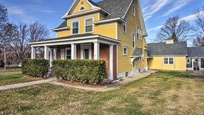 A two-story yellow house with a front porch, brick foundation, and a chimney.