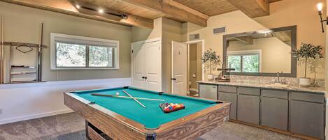 Une table de billard dans une pièce avec des poutres en bois, un coin cuisine et un grand miroir.