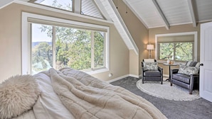 A bedroom with a large window, a ceiling fan, and a cozy seating area with a lamp.