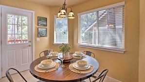 A dining room with a round table set for four, surrounded by chairs, with a chandelier above.