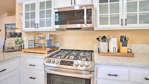 A kitchen with white cabinetry, a stainless steel stove, a microwave, and various kitchen utensils.