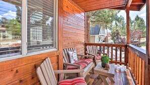 A wooden porch with a bench and chairs, a table with a plant, and a view of the surrounding area.