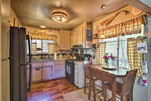 Una cocina con piso de madera, estufa, refrigerador y una mesa de comedor con sillas.