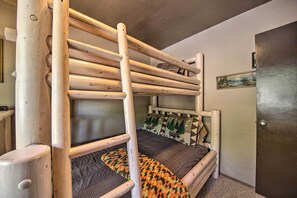 A bunk bed with a wooden ladder, a patterned rug, and a door with a painting on the wall. - Family Cabin w/ Game Room Near Hiking + Skiing! (Lake Arrowhead)