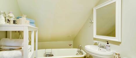 A bathroom with a bathtub, a sink, and a mirror. There are towels stacked on shelves and a basket with toiletries.