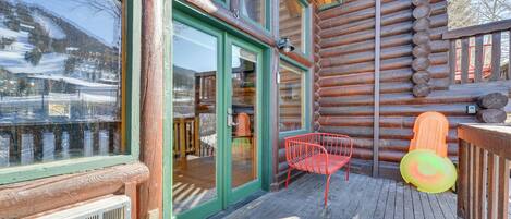 Una cabaña de troncos con una terraza de madera, una puerta de cristal y una silla roja.