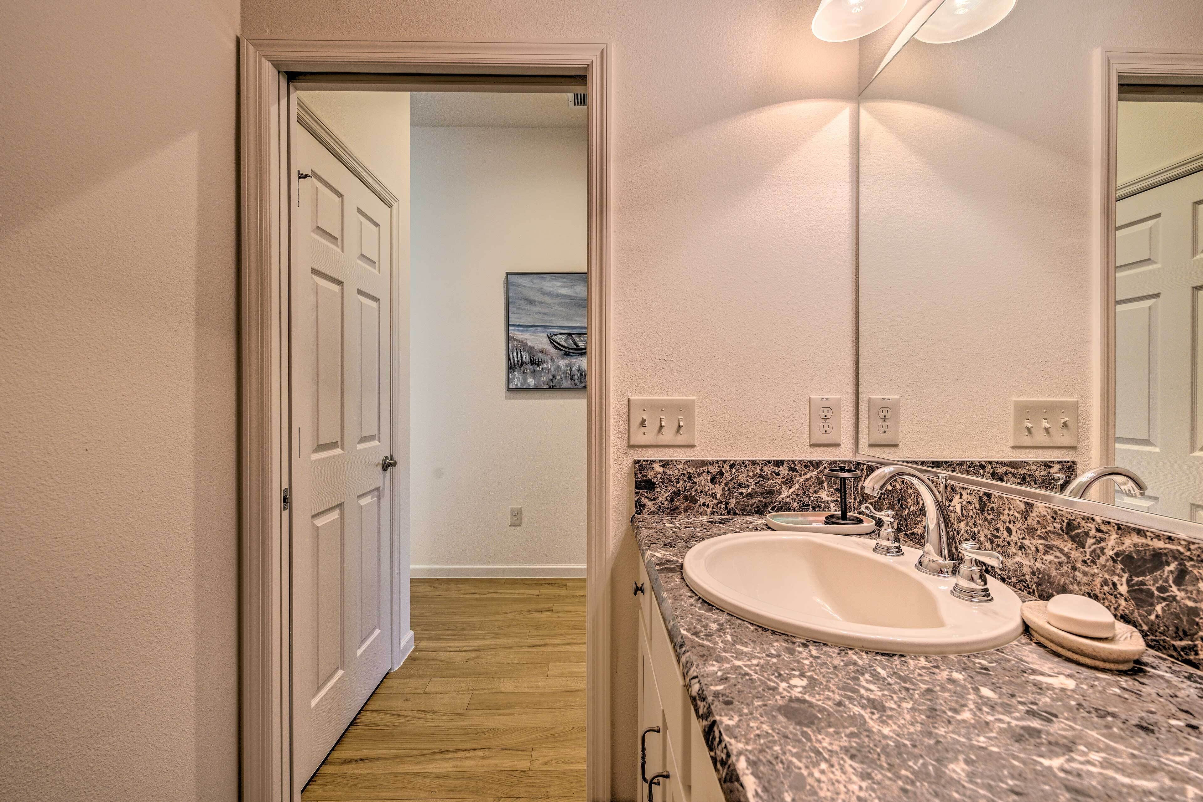 A bathroom with a white sink, granite countertop, and a large mirror.