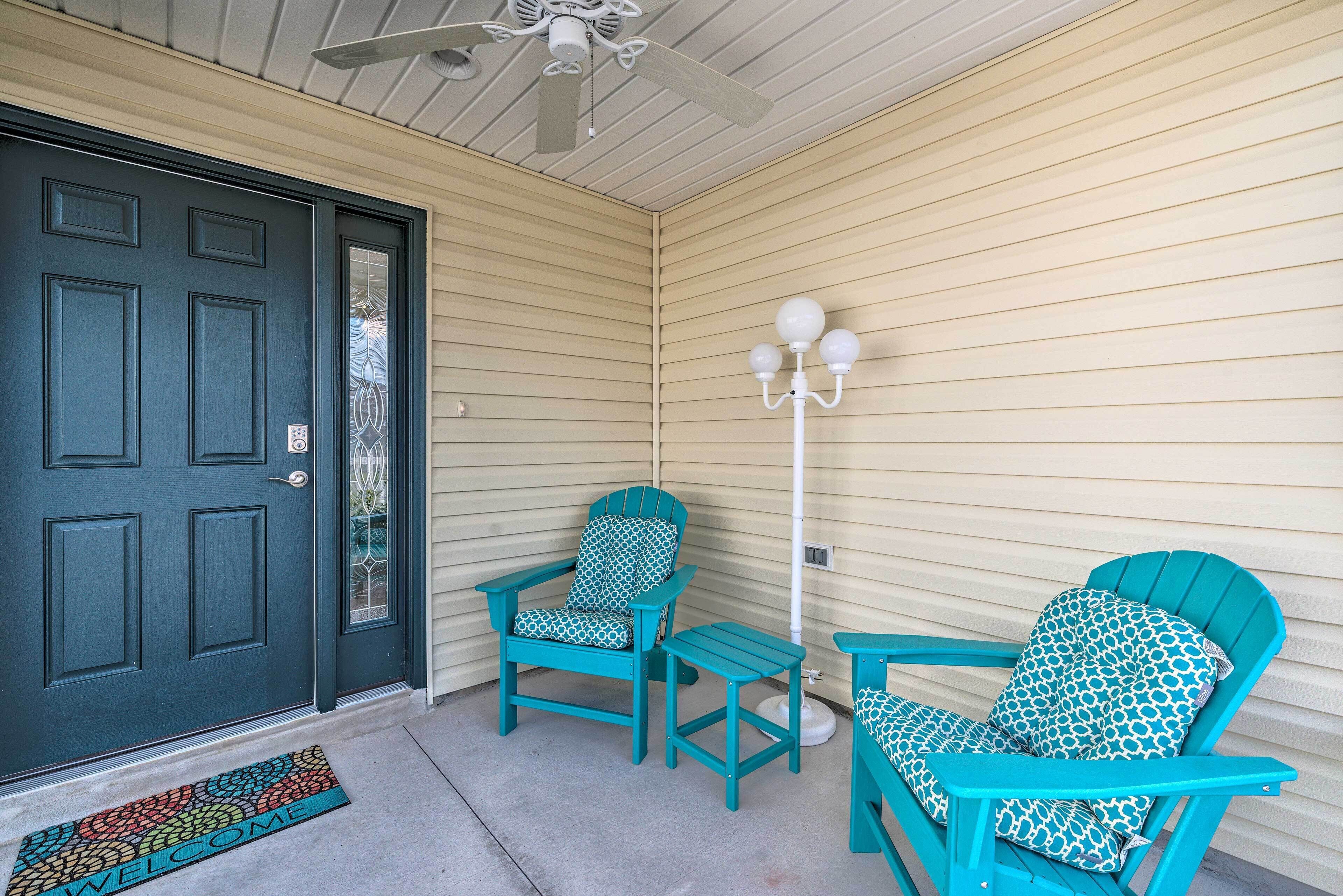 A porch with two teal Adirondack chairs, a small table, and a white floor lamp.