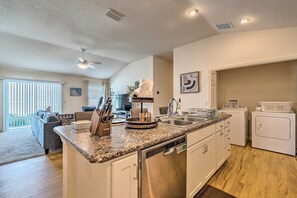 A modern kitchen with granite countertops, stainless steel appliances, and a dishwasher. There is a dining area with a gray sofa and a dining table. - Golfer's Paradise - The Villages in Wildwood! (Wildwood)