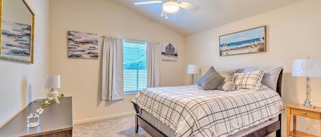 A bedroom with a bed, ceiling fan, and artwork on the walls.