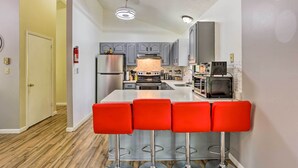 Une cuisine moderne avec des meubles gris, un réfrigérateur en acier inoxydable, un four à micro-ondes et un grille-pain. On trouve quatre tabourets de bar rouges devant l’îlot central de la cuisine.