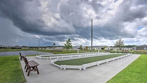 Un campo de croquet con bancos y un estanque al fondo.