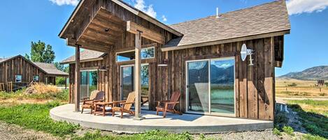 A wooden cabin with a covered patio, large sliding glass doors, and a view of the landscape.