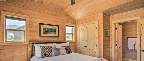 Une chambre à coucher dans une cabane en bois, avec un lit, des oreillers, un ventilateur de plafond et une porte donnant accès à une salle de bain.