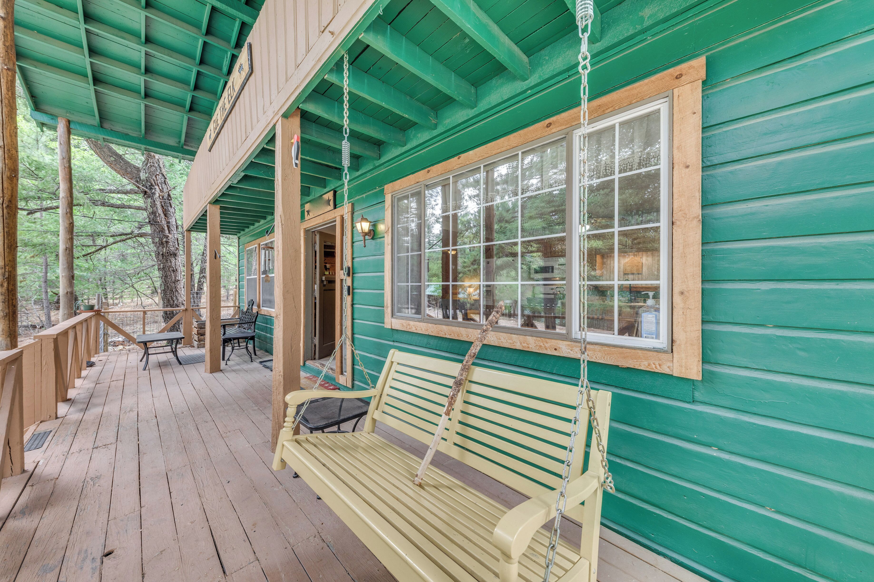 A wooden deck with a bench and tables, a covered area with a green roof, and a large window.
