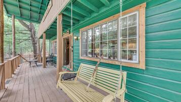 A wooden deck with a bench and tables, a covered area with a green roof, and a large window.