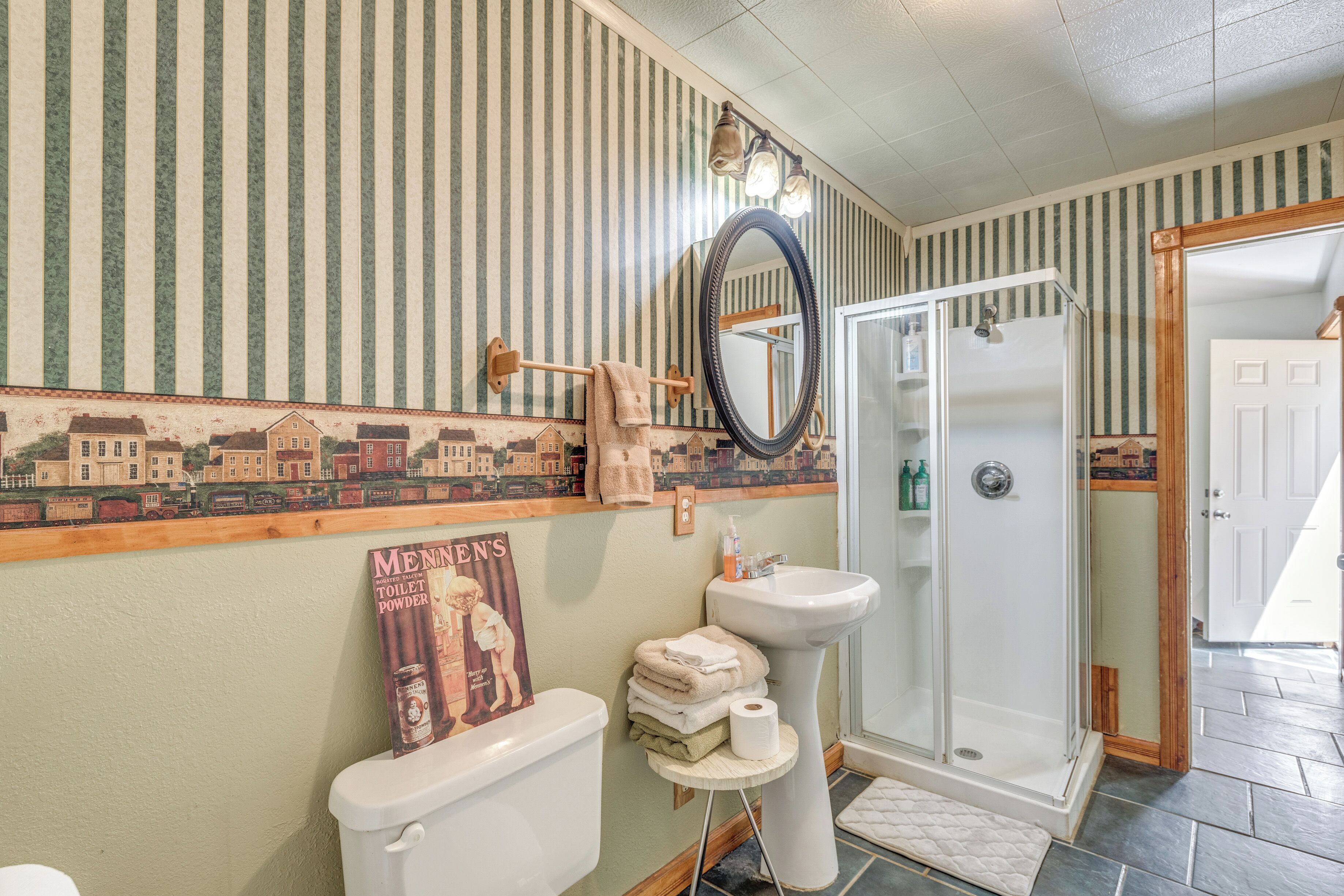 A bathroom with a striped wall, a toilet, a sink, a shower, and a mirror.