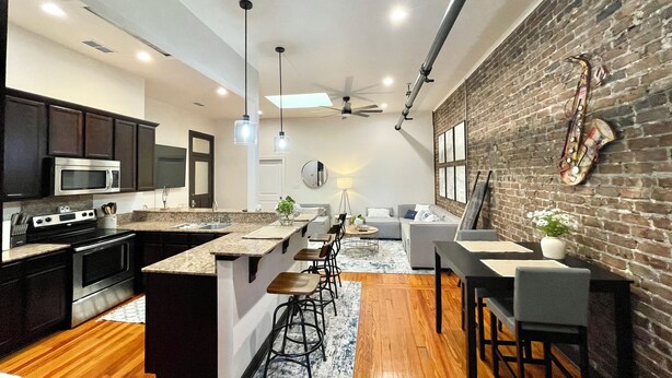 Una cocina moderna con armarios oscuros, una isla central y un comedor con pared de ladrillo y una decoración con saxofón.