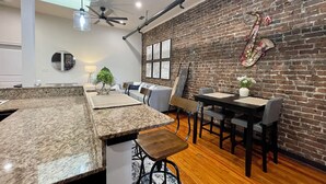 Una cocina moderna con encimeras de granito, un comedor con pared de ladrillo y un ventilador de techo.
