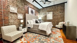Un dormitorio con pared de ladrillo, una cama, una silla y un escritorio.