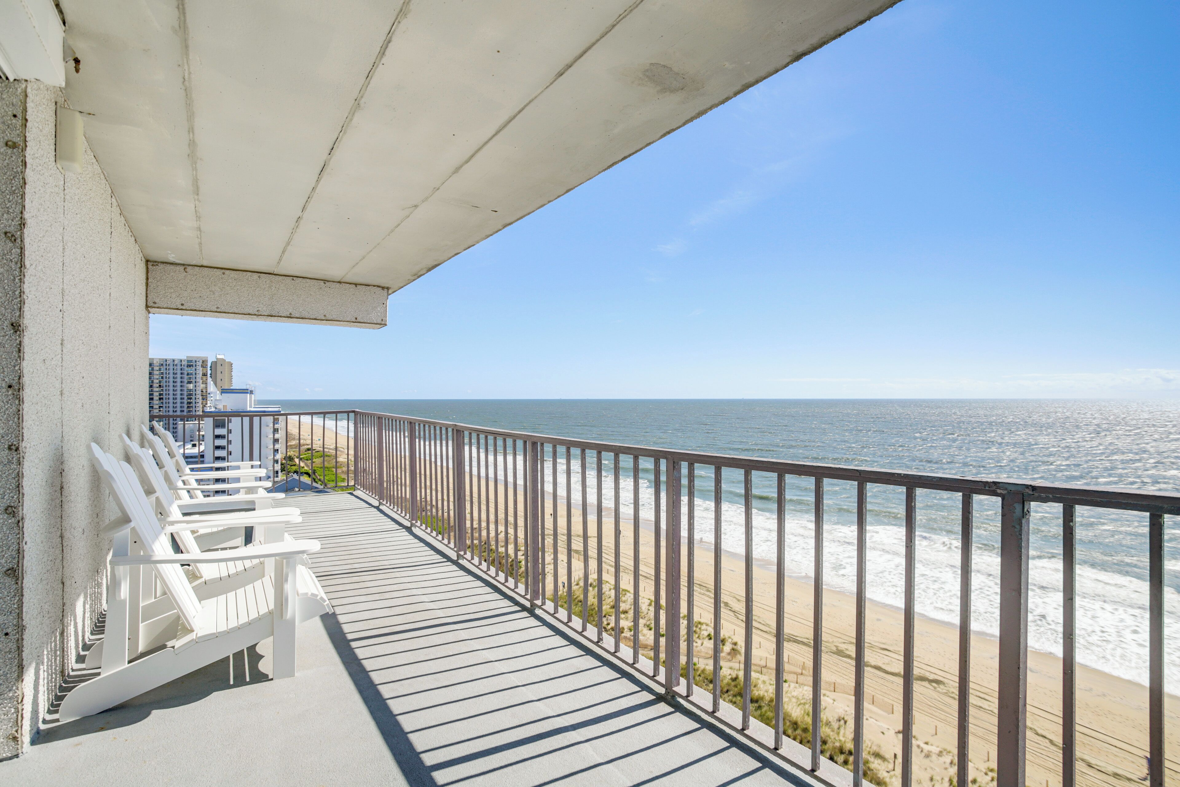 A balcony with white chairs overlooking a beach and ocean.