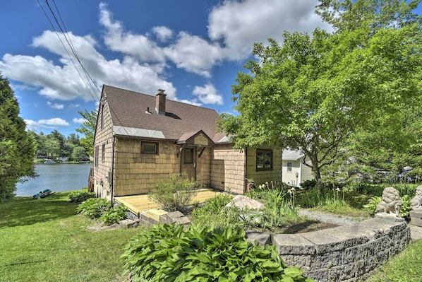 A two-story house with a stone exterior, a front porch, and a view of a lake. - Picturesque Cottage With Sunroom on Ashmere Lake! (Hinsdale)