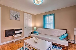 Una sala de estar con un sofá blanco, una mesita pequeña, un adorno en la pared, una cortina azul y una lámpara.