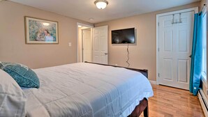 A bedroom with a bed, a painting, a television, and a door. - Cozy Third-story Apartment in Dtwn Brockton! (Brockton)