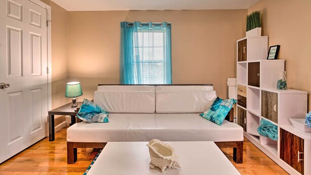 A room with a white sofa, a small table with a lamp, a white cabinet with shelves, and a door. - Cozy Third-story Apartment in Dtwn Brockton! (Brockton)