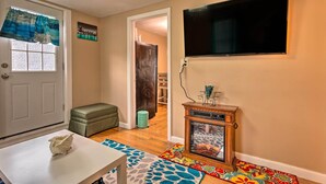 A room with a white door, a green bench, a television mounted on the wall, and a small wooden cabinet with a glass door. - Cozy Third-story Apartment in Dtwn Brockton! (Brockton)
