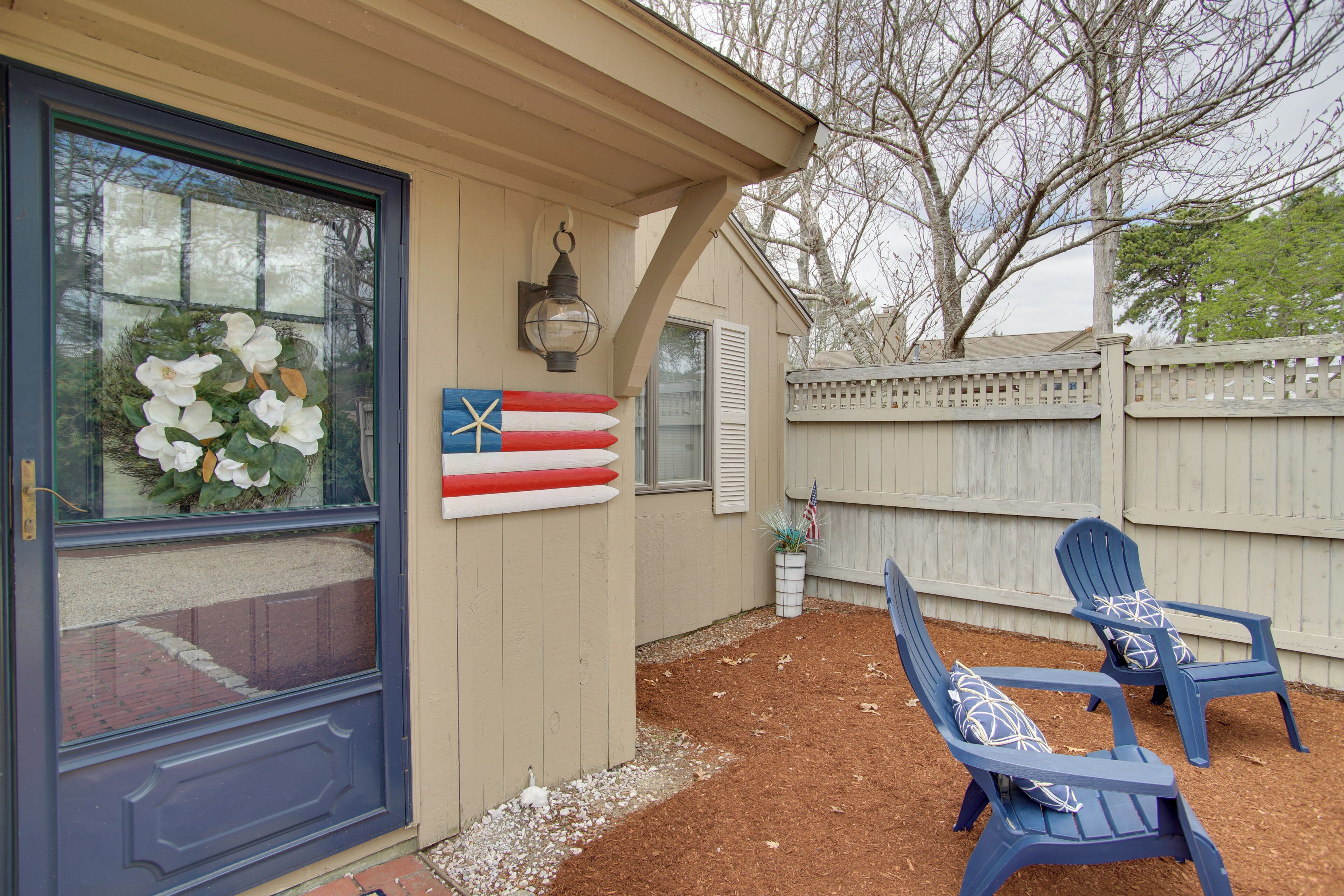A house with a front door, a window with a wreath, and two blue Adirondack chairs with pillows.