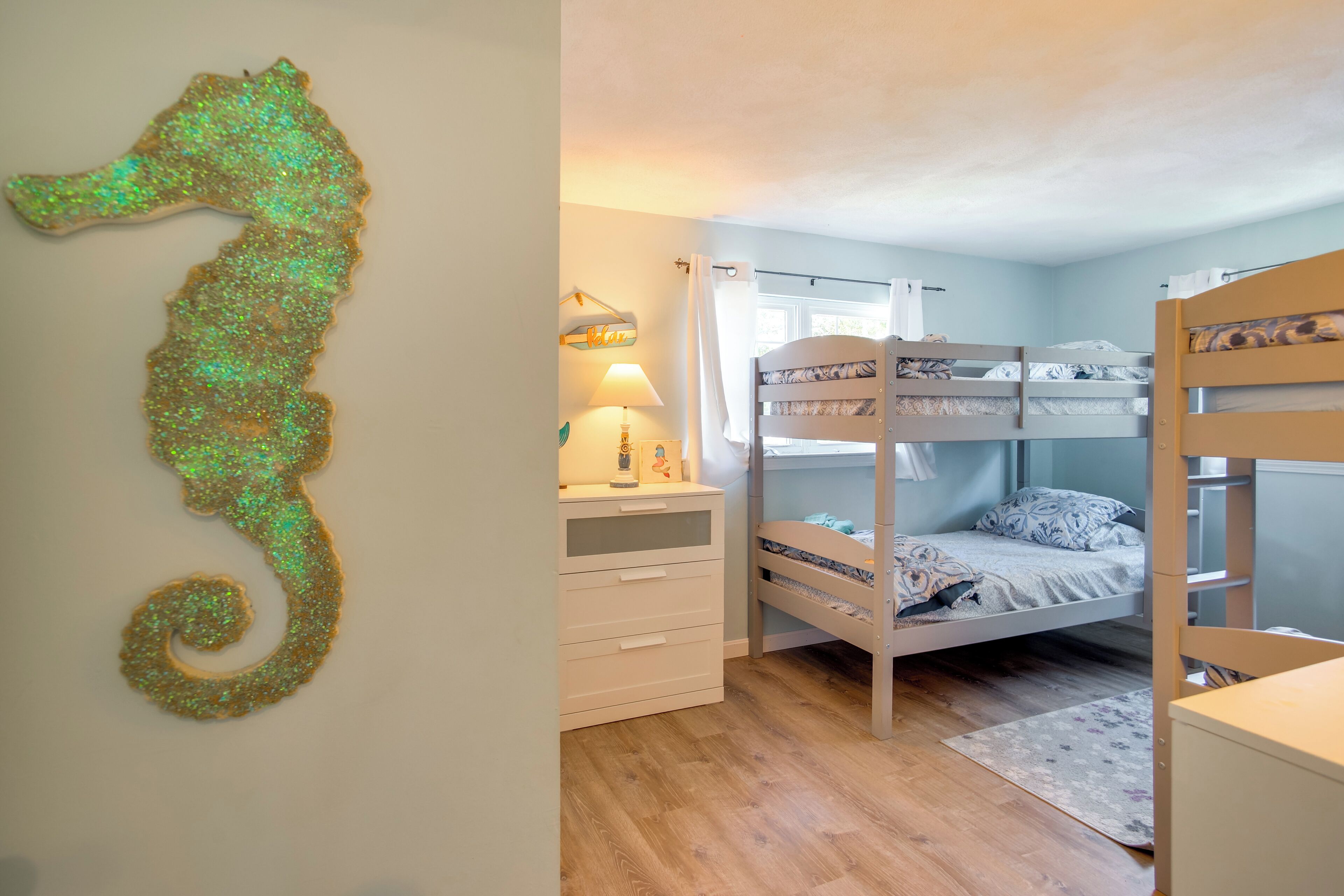 Una habitación con literas, un escritorio con lámpara y una decoración de caballito de mar en la pared.
