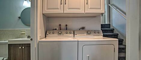 A compact laundry room with a front-loading washer and dryer, wooden cabinets, and a small countertop with a sink.