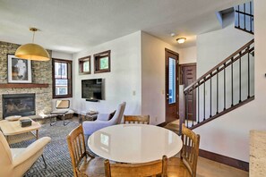 A spacious living room with a fireplace, a round dining table, and a staircase.