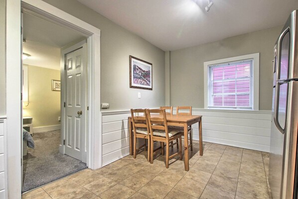 A dining area with a wooden table and chairs, a window with blinds, and a refrigerator.