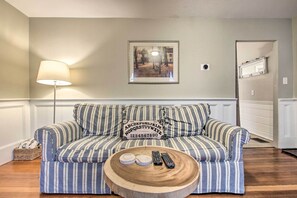 A striped sofa with pillows, a round wooden coffee table, and a lamp in a room with a framed picture on the wall. - Inviting Salem Apartment Near Waterfront & Museums (Salem)