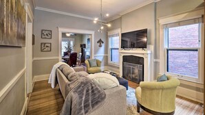 A living room with a fireplace, a sofa, a chair, and a TV mounted on the wall. - Louisville Home w/ Hot Tub in The Highlands! (Louisville)