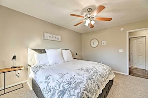 A bedroom with a bed, a ceiling fan, a bedside table with a lamp, and a door.