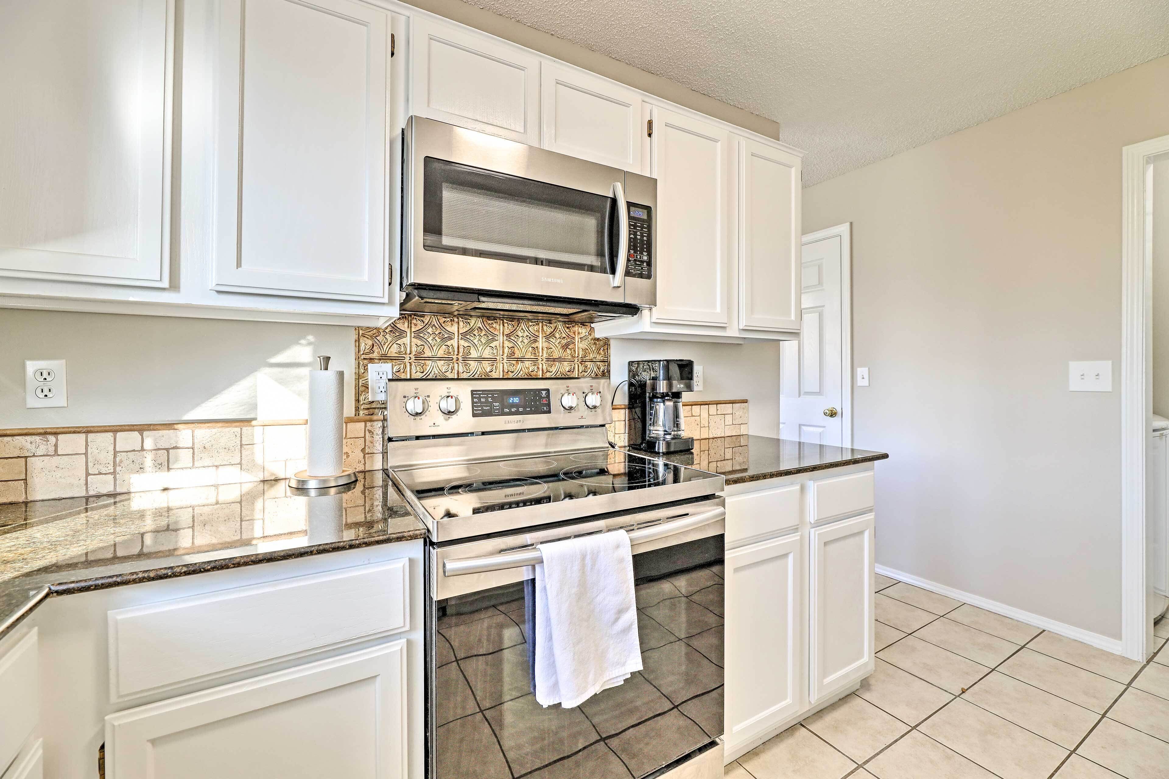 A kitchen with white cabinets, a stainless steel stove, a microwave, and a coffee maker.