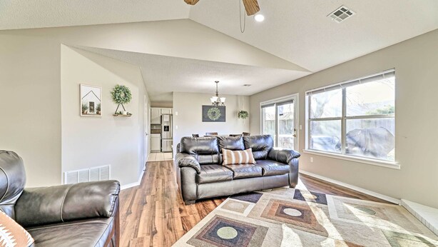 A spacious living room with a leather sofa, a patterned rug, and a large window providing natural light. - Fayetteville Home w/ Hot Tub ~ 3 Mi to U of A! (Fayetteville)