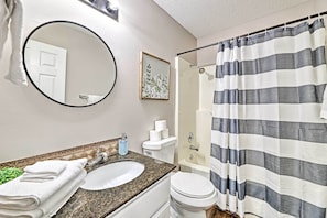 Un baño con un espejo redondo, un lavabo, un inodoro y una cortina de ducha.