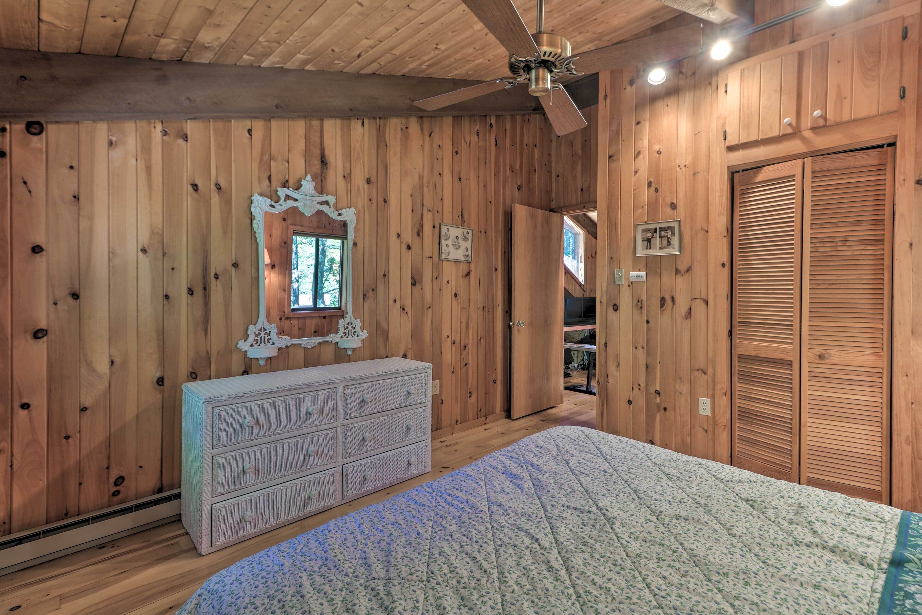 A wooden-paneled bedroom with a bed, dresser, and a ceiling fan.