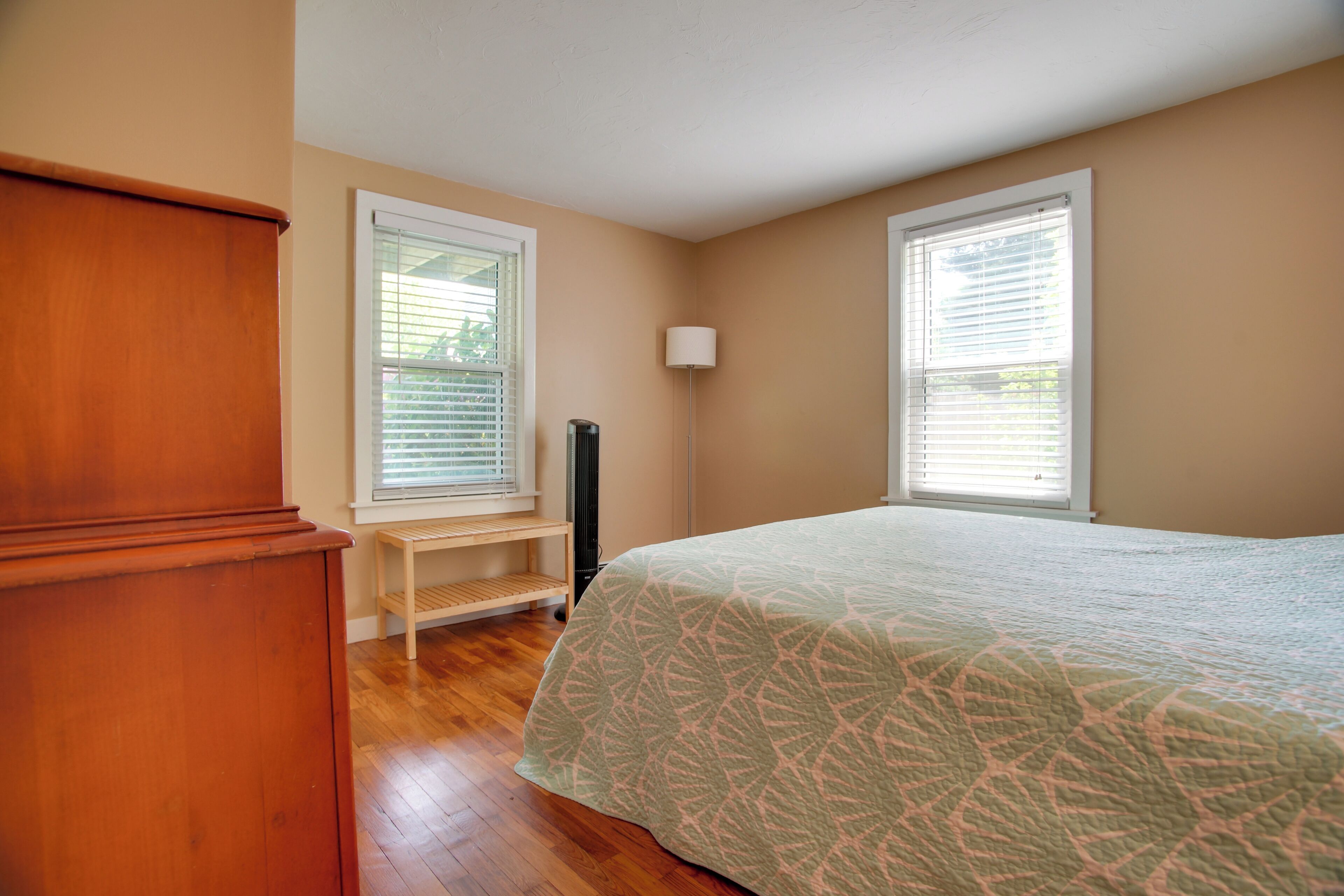 Quarto com cama, piso de madeira, um banco e uma luminária.