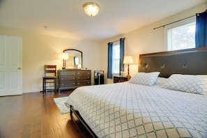 A bedroom with a large bed, a dresser, a mirror, and a nightstand with a lamp.