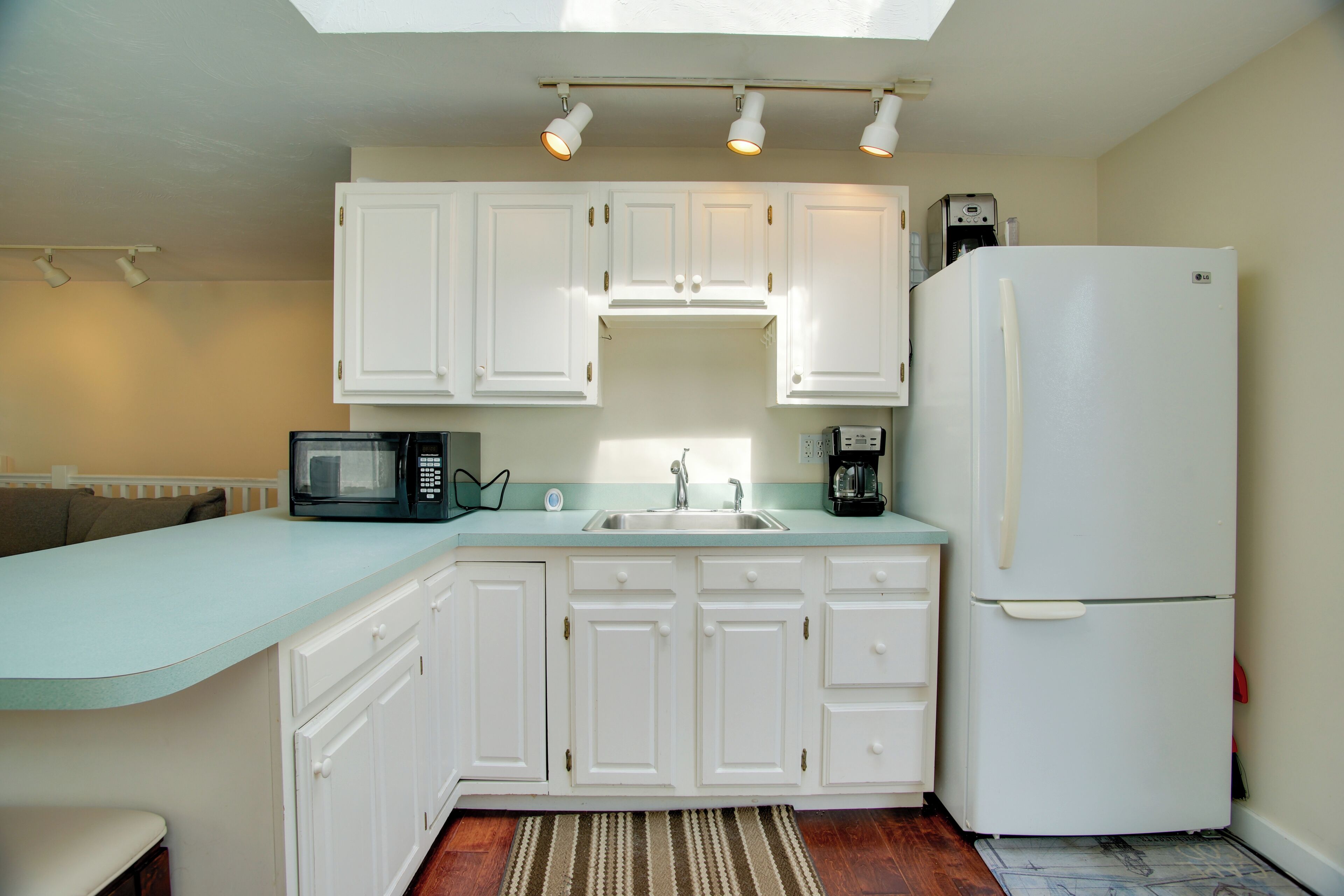 A kitchen with white cabinets, a microwave, a coffee maker, and a refrigerator.