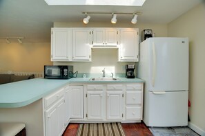 A kitchen with white cabinets, a microwave, a coffee maker, and a refrigerator. - < 1 Mi to Beach: Family-friendly Falmouth Home! (Falmouth)