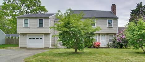 A two-story house with a garage, a lawn, and a tree in front.
