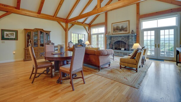 A spacious room with wooden beams, a fireplace, a dining area with a table and chairs, and large windows. - Luxury Vacation Rental in the Berkshires! (Williamstown)
