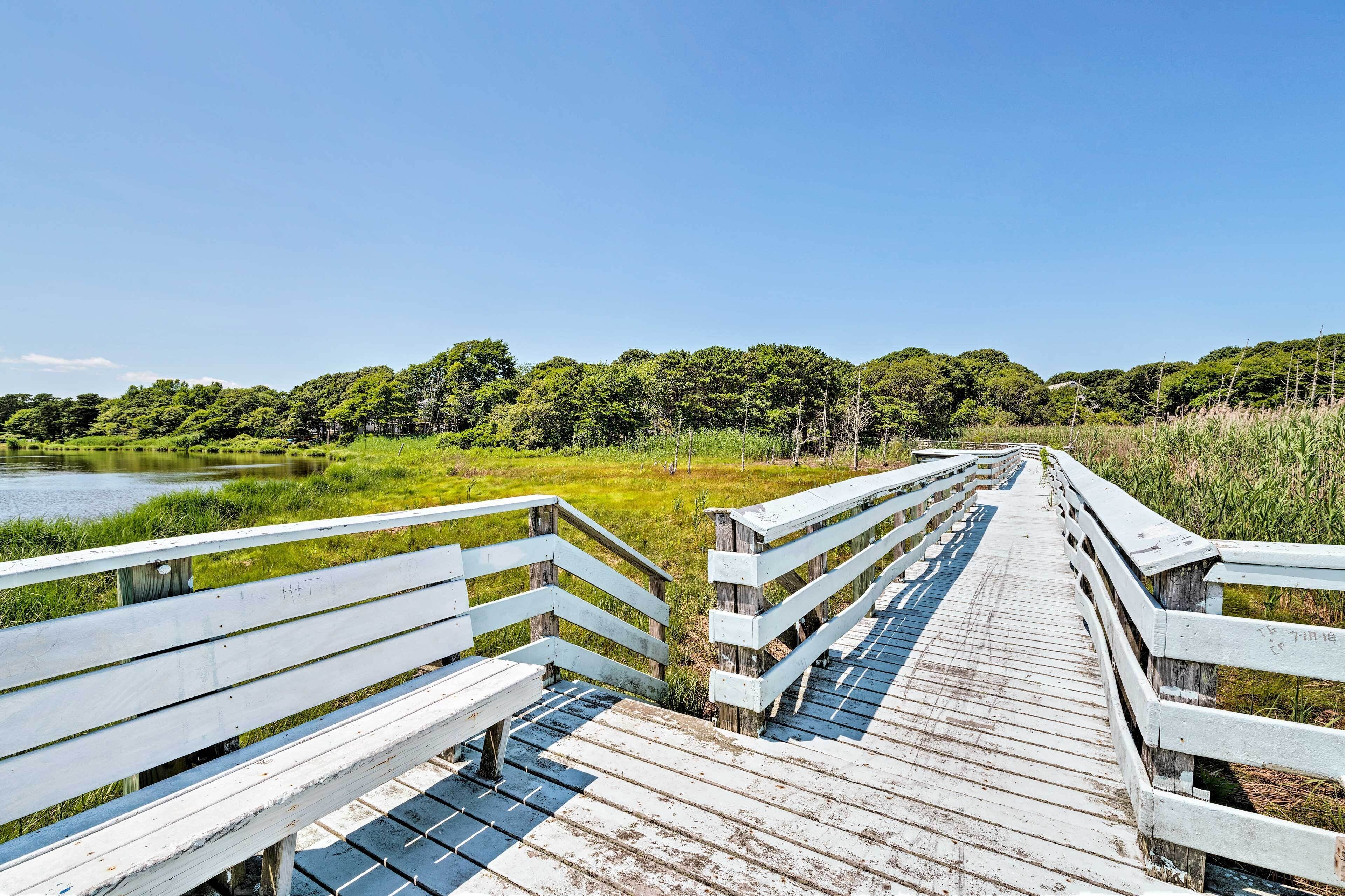 A wooden boardwalk leading to a body of water, surrounded by greenery and trees.